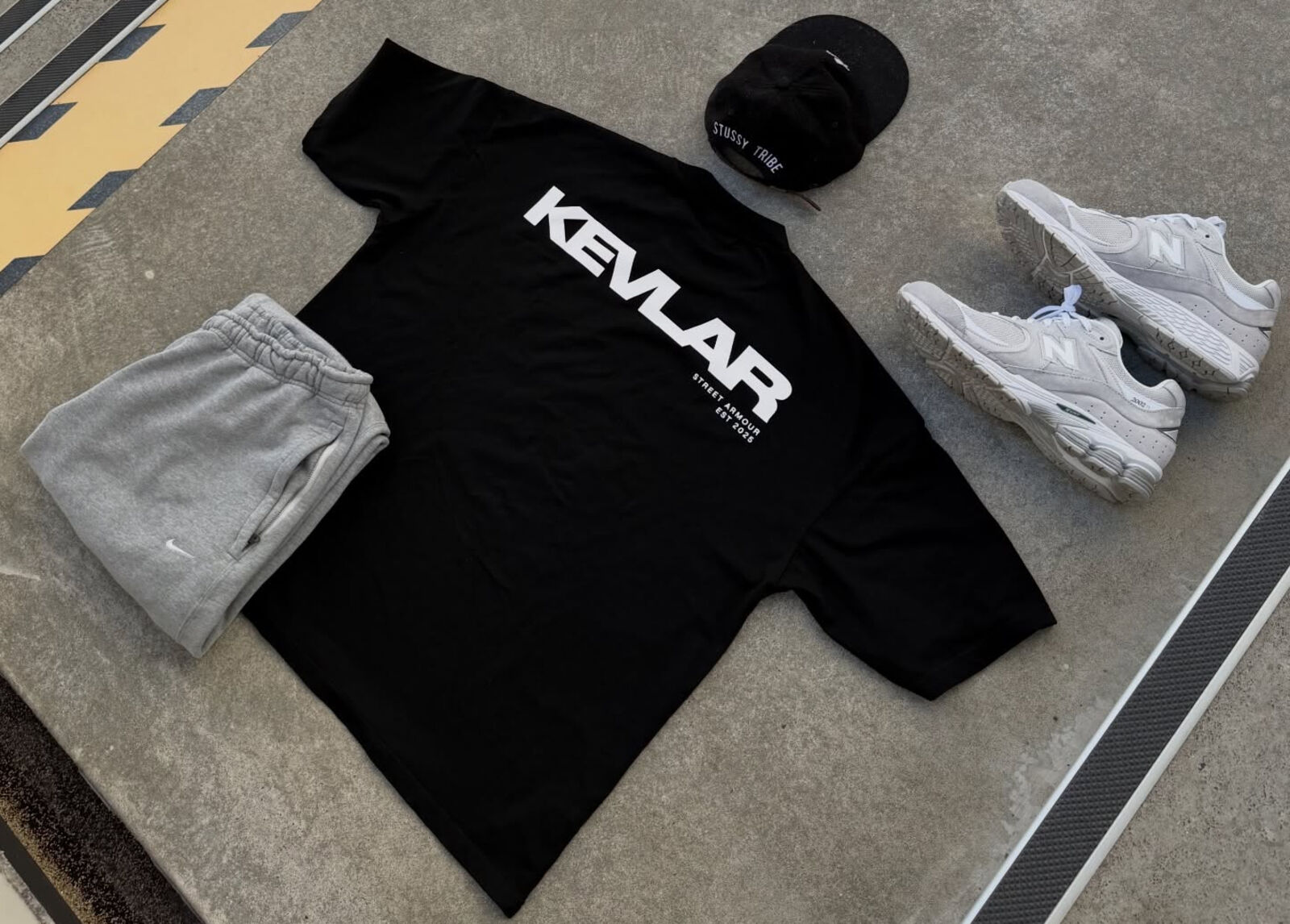 KEVLAR Studio V1 Tee flat-lay with sweats, cap and sneakers on Auckland concrete